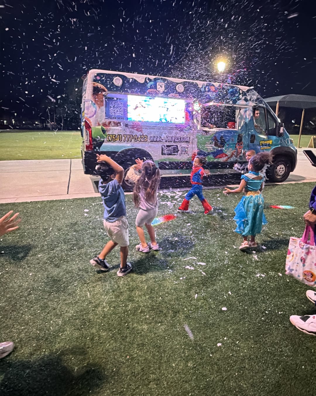 Kids in costumes in falling snow in front of the Zombie Ice truck at night